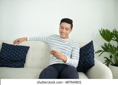 Young Handsome Asian Man Using Modern Mobile Smart Phone Sitting On A Couch At Home