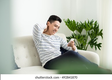 Young Handsome Asian Man Using Modern Mobile Smart Phone Sitting On A Couch At Home