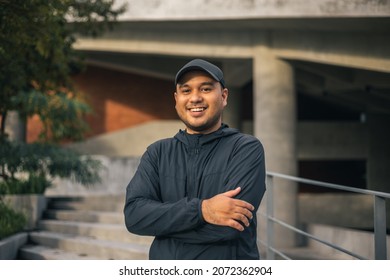 Young handsome asian man wearing sportswear standing post under the building urban city running outdoor. Portraits of Indian man jogging on the road. Training athlete outdoor concept.