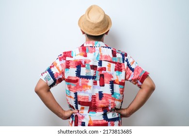 Young Handsome Asian Man Wearing Casual Beach Shirt And Bucket Hat Over White Background Standing Backwards Looking Away With Arms On Body Isolated Over White Background