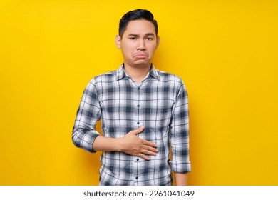 Young handsome Asian man wearing casual clothes keeps his hands on his stomach feeling hungry and wanting to eat delicious isolated on yellow background. People lifestyle concept