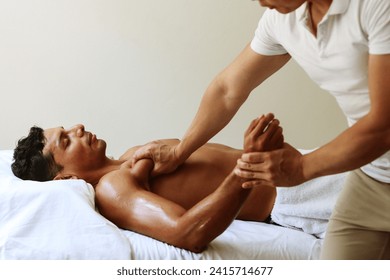 young handsome asian massage therapist perform massage on pectoralis for young muscular man who lying on the massage table in the supine position. White room background. - Powered by Shutterstock