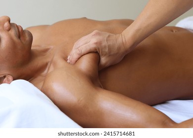 young handsome asian massage therapist perform massage on pectoralis for young muscular man who lying on the massage table in the supine position. White room background. - Powered by Shutterstock