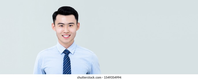 Young Handsome Asian Professional Man In Business Shirt And Tie With Fresh Clean Shaven Appearance Facing Camera And Smiling Isolated On Light Gray Banner Background