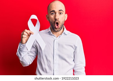 Young Handsome Bald Man Holding White Cancer Ribbon Scared And Amazed With Open Mouth For Surprise, Disbelief Face 