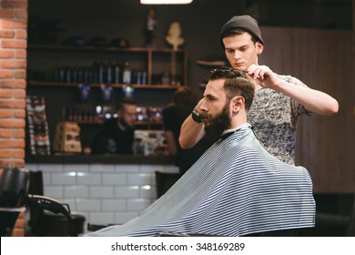 Young handsome barber making haircut of attractive bearded man in barbershop - Powered by Shutterstock