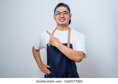 Young handsome barista man wearing apron standing over isolated white background with a big smile on face, pointing with hand and finger to the side looking at the camera. - Powered by Shutterstock