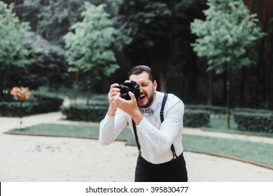 Young handsome beard man in white shirt and trousers makes beautiful pictures on film retro camera, stylishly dressed, photographer,outdoor portrait, close up,brutal, tattoo, street photo,photographer
