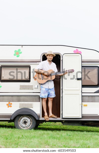 Young and handsome bearded guy playing\
guitar outdoors. Holiday, journey, vacation\
concept.