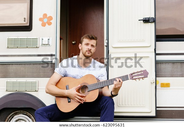 Young and handsome bearded guy playing
guitar outdoors. Holiday, journey, vacation
concept.