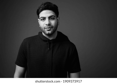 Young handsome bearded Indian man against gray background