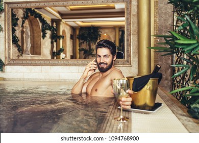 Young Handsome Bearded Man Enjoying And Relaxing In Spa Center. He Sitting In Hot Tub And Drinking Wine.