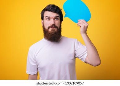 Young handsome  bearded man holding blank paper speech bubble in hands over yellow background - Shutterstock ID 1302109057