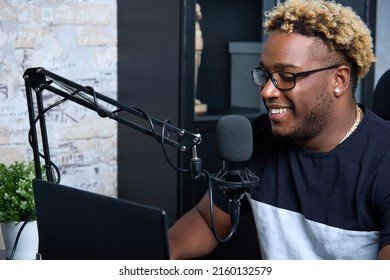 A Young And Handsome Black DJ With Glasses Plays Music In His Home Studio. A Stylish Professional Presenter Smiles During A Live Broadcast, Conducts A Fascinating Conversation With The Audience