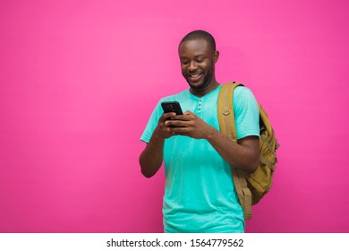 Young handsome black man carrying a backpack and smiling while pressing his phone