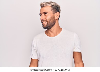 Young handsome blond man wearing casual t-shirt standing over isolated white background looking to side, relax profile pose with natural face and confident smile.