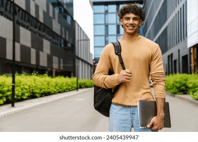 Young handsome business man in casual wear smiling at camera while standing outdoors near office buildings - Powered by Shutterstock