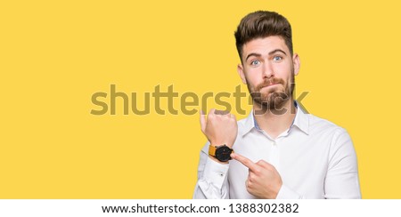 Young handsome business man In hurry pointing to watch time, impatience, upset and angry for deadline delay