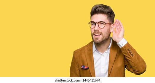 Young handsome business man wearing glasses smiling with hand over ear listening an hearing to rumor or gossip. Deafness concept. - Shutterstock ID 1446411674