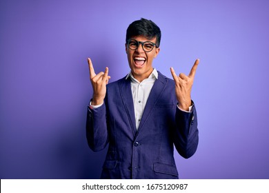 Young Handsome Business Man Wearing Jacket And Glasses Over Isolated Purple Background Shouting With Crazy Expression Doing Rock Symbol With Hands Up. Music Star. Heavy Music Concept.