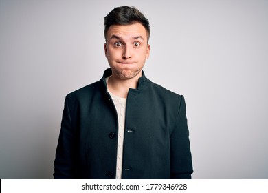 Young Handsome Business Mas Wearing Elegant Winter Coat Standing Over Isolated Background Puffing Cheeks With Funny Face. Mouth Inflated With Air, Crazy Expression.