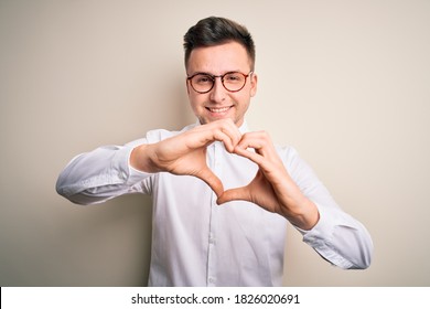 Young Handsome Business Mas Wearing Glasses And Elegant Shirt Over Isolated Background Smiling In Love Doing Heart Symbol Shape With Hands. Romantic Concept.