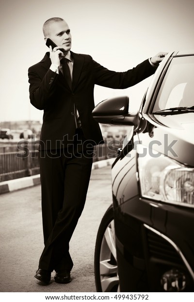 Young handsome businessman calling on cell phone next\
to his car