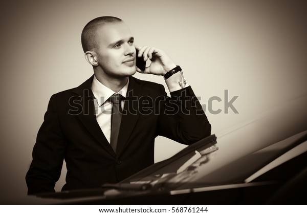 Young handsome businessman calling on mobile phone next\
to his car  