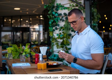 Young Handsome Businessman Eating In A Restaurant While Using Airpods