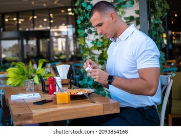 Young Handsome Businessman Eating In A Restaurant While Using Airpods