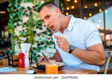 Young Handsome Businessman Eating In A Restaurant While Using Airpods