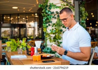 Young Handsome Businessman Eating In A Restaurant While Using Airpods