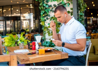 Young Handsome Businessman Eating In A Restaurant While Using Airpods