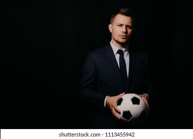 Young Handsome Businessman Holding A Football On Black Background Studio. Blue Jacket And Tie. Stylish Hairstyle Model. World Championship.