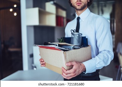 Young handsome businessman in light modern office with carton box. Last day at work. Upset office worker is fired.