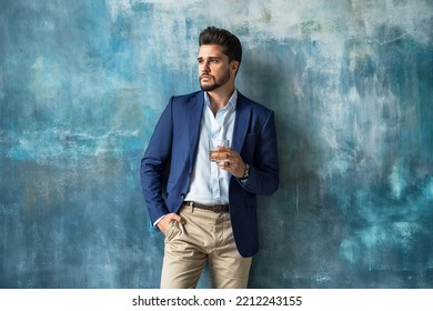 Young handsome businessman posing in elegant fashionable clothes, holding a glass of whiskey, tkinking and looking away. Portrait of bearded man. A lot of copy space on the background.  - Shutterstock ID 2212243155