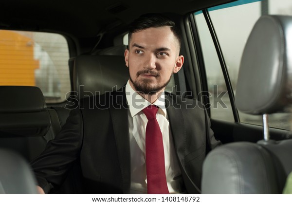 Young\
handsome businessman sitting in the car. Portrait of New owner of\
luxury car - Bearded man wearing formal\
suit