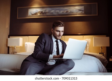 Young handsome businessman talks on-line with his business partners at the hotel room. Hotel service. Booking hotel. Freelancer sitting on his sofa in a hotel room and working with his computer.  - Shutterstock ID 709011313