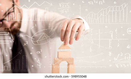 Young handsome businessman using wooden building blocks with white calculations scribbled around him