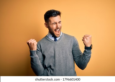 Young handsome businessman wearing elegant sweater and tie over yellow background very happy and excited doing winner gesture with arms raised, smiling and screaming for success. Celebration concept. - Powered by Shutterstock