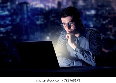 Young Handsome Businessman Working Late At Night In The Office With Blue Lights In The Background