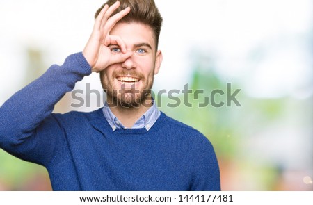 Young handsome bussines man doing ok gesture with hand smiling, eye looking through fingers with happy face.