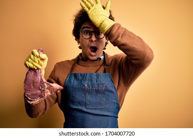 Young Handsome Butcher Man Holding Meet Steak Standing Over Isolated Yellow Background Surprised With Hand On Head For Mistake, Remember Error. Forgot, Bad Memory Concept.