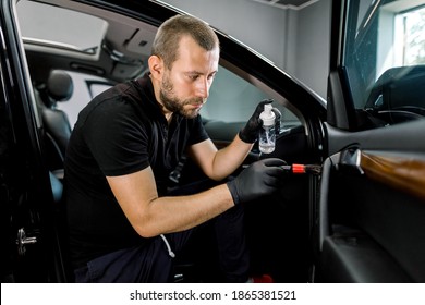 Young handsome car detailing worker making professional cleaning and remowing of the dust of car interior, using special cleansing disinfecting foam and soft brush. Car interior cleaning