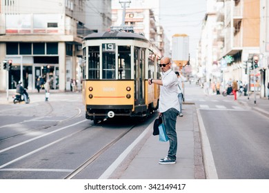 Young handsome caucasian bald business man standing on a bus stop, looking down his wrist watch - delay, work, waiting concept