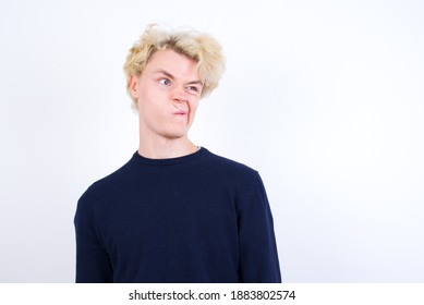 Young handsome Caucasian blond man standing against white background making grimace and crazy face, screaming out of control, funny lunatic expressing freedom and wild.