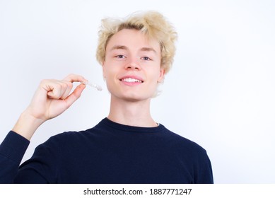 Young handsome Caucasian blond man standing against white background holding an invisible aligner or retainer and smiling.  Dental healthcare concept and recommendation. 