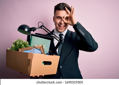 Young handsome caucasian business man holding cardboard box unemployment fired from job with happy face smiling doing ok sign with hand on eye looking through fingers