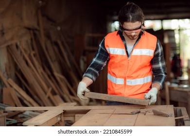 Young And Handsome Caucasian Carpenter Craftsman In The Carpentry Shop Wearing Safety Uniform Workwear Is Holding And Check The Plank For Furniture Repair. Small Business And Freelance Craftsman.