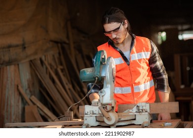 Young And Handsome Caucasian Carpenter Craftsman In Carpentry Shop Wearing Safety Uniform Workwear Use Circular Saws To Cut Wood Board To Make Furniture. Small Business And Freelance Craftsman